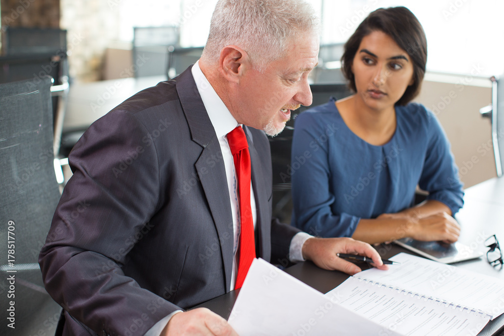Serious businessman explaining papers to intern Serious businessman explaining papers to intern