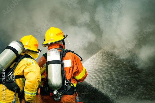 two firefighters water spray by high pressure nozzle to fire surround with smoke and copy space