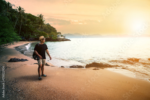 traveling man and dslr camera walking on sand beach against sunset sky