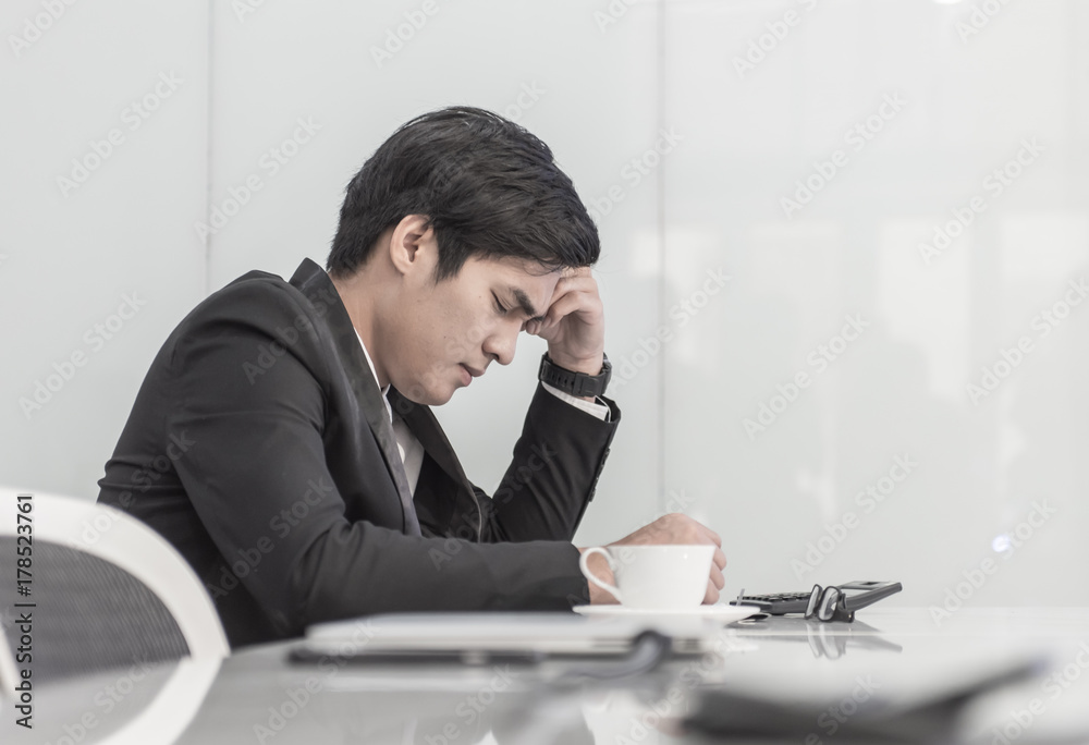 businessman having a hard time with coin stack, calculator and document graphic on the table, he holding his head in his hands. businessman having a hard time with coin stack, calculator and document graphic on the table, he holding his head in his hands.