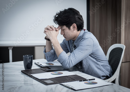 businessman having a hard time with coin stack, calculator and document graphic on the table, he holding his head in his hands.