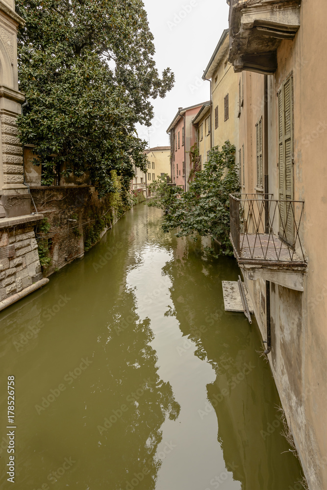 lush vegetation and old houses on  Rio canal in city center, Mantua, Italy