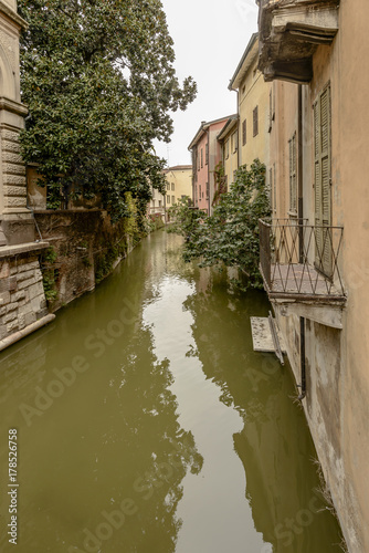 lush vegetation and old houses on Rio canal in city center, Mantua, Italy