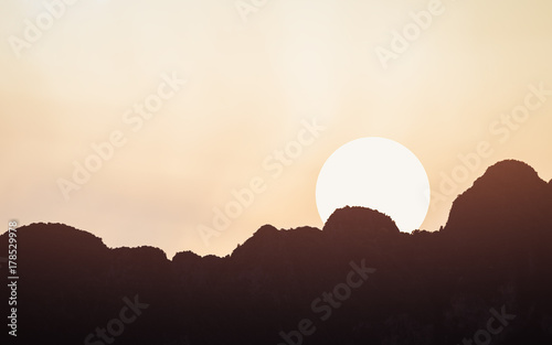 Sunset scene of moving sun over the edge of silhouetted dark mountains range with clear orange warm sky.