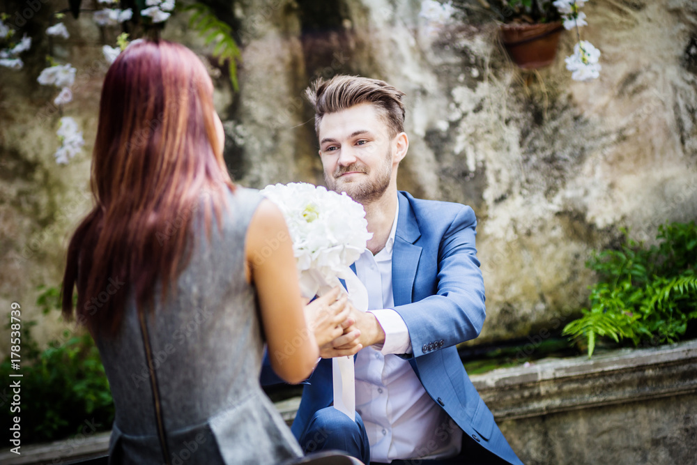 Portrait Young man proposing to millennial girlfriend in garden with white flower