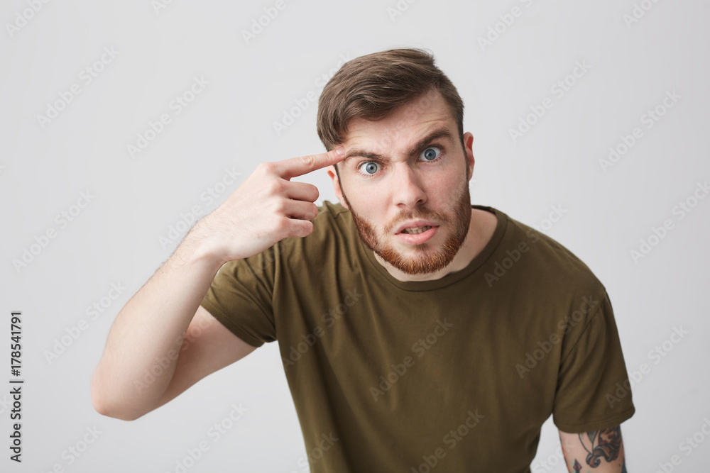 Close up portrait of negative young good-looking bearded tattooed european man with short brown hair in casual colorful t-shirt arguing with friend in university with angry and mean expression Close up portrait of negative young good-looking bearded tattooed european man with short brown hair in casual colorful t-shirt arguing with friend in university with angry and mean expression