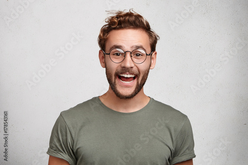 Funny smiling unshaven male wonk wears round spectacles and casual clothes, being glad to recieve interesting book as present, expresses positive emotions. People, happiness, positiveness concept