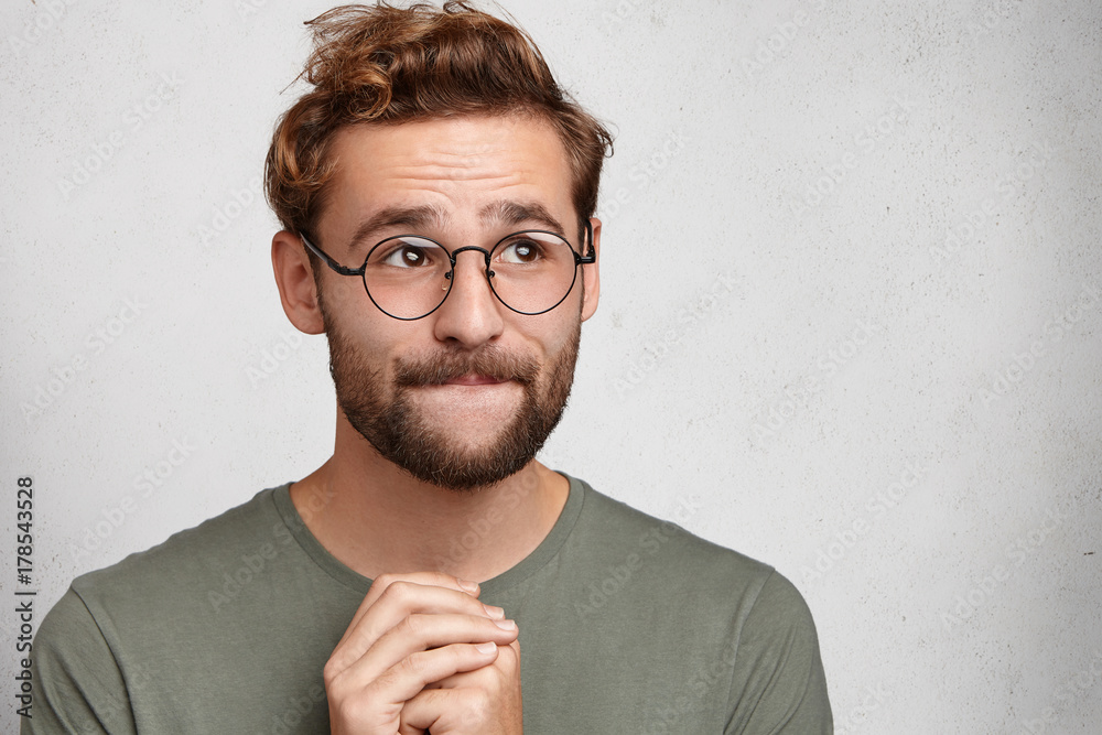Indoor shot of pleasant looking man keeps palms together, has hopeful inspired look, asks for good luck before important event. Male student weara spectacles being clueless, believes in fortune Indoor shot of pleasant looking man keeps palms together, has hopeful inspired look, asks for good luck before important event. Male student weara spectacles being clueless, believes in fortune