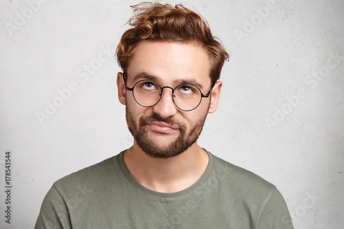 Portrait of stylish bearded man with bored fed up expression, looks displeased up, being tired to explain new material to his friend who can`t understand it. Puzzled male doesn`t know what to do