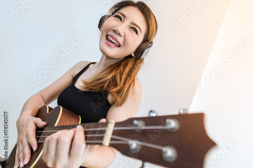 beautiful Asian Woman Playing Ukulele with happiness and joyful near widow white room background photo