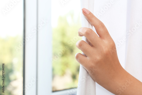 Woman drawing white curtains indoors, closeup