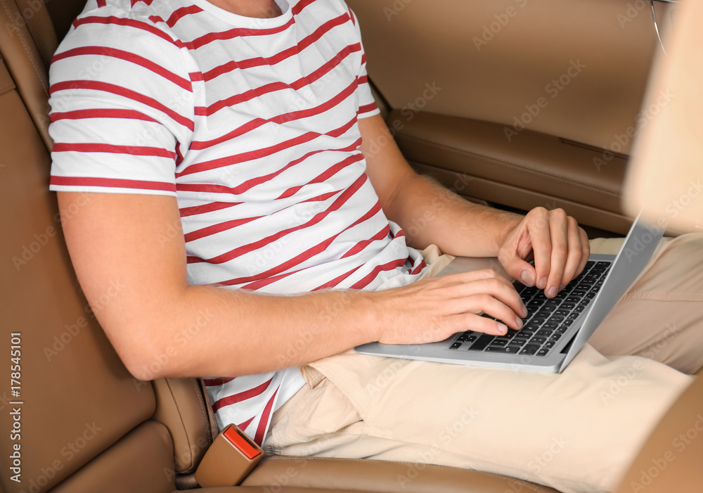 Fototapeta premium Handsome young man with laptop on backseat of car