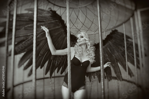 blond woman with black wings in a cage. Angel, mysticism