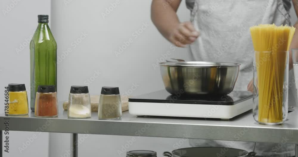 Male chef puts a pan on the stove and pours water in an industrial style kitchen with spaghetti and spices Male chef puts a pan on the stove and pours water in an industrial style kitchen with spaghetti and spices