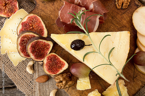 cheese plate with pieces moldy cheese, prosciutto, pickled plums, olives, grapes, figs, honey, pear,  walnuts, almonds, cashews on old wooden background. Rustic style. photo