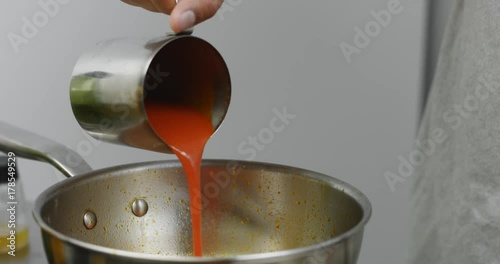 Close up of pouring thick tomato sauce into hot olive oil with paprika in a stainless steel saucepan