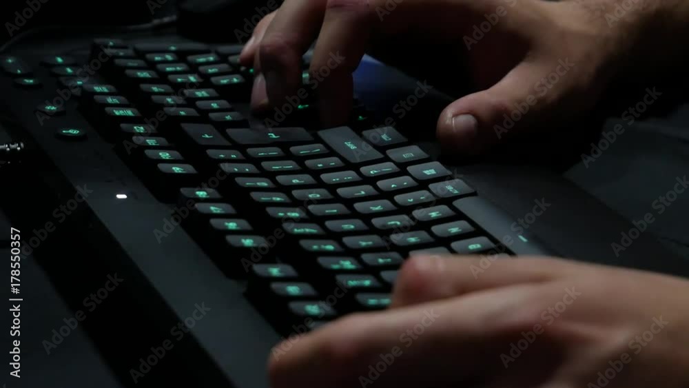 Man hands typing on a gaming computer keyboard. Keyboard with green-blue light. Neon light.