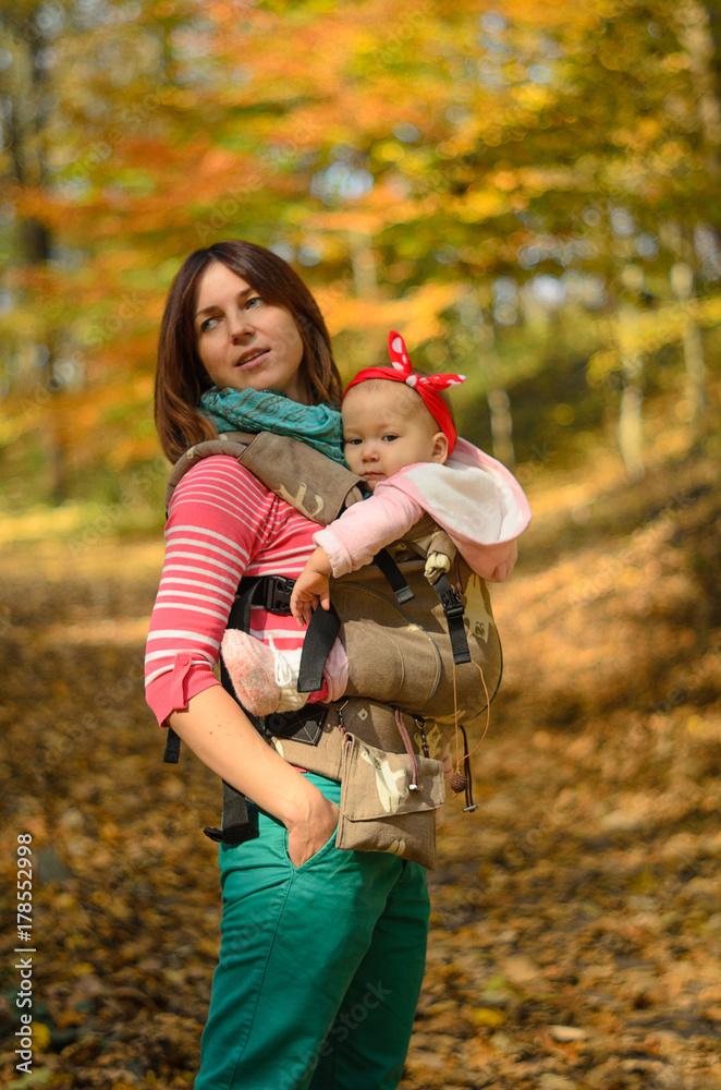 Mother carrying her baby daughter in ergonomic backpack for children