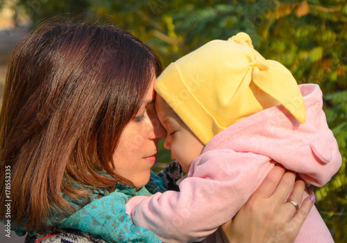 Obraz na płótnie Young mother holding her baby touching her with forehead and closed eyes. Deep feeling of love. w salonie