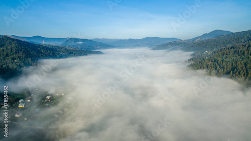 Aerial photography morning fog over mountainous town. Aerial landscape view of the town and top of the mountains from the height of the bird on