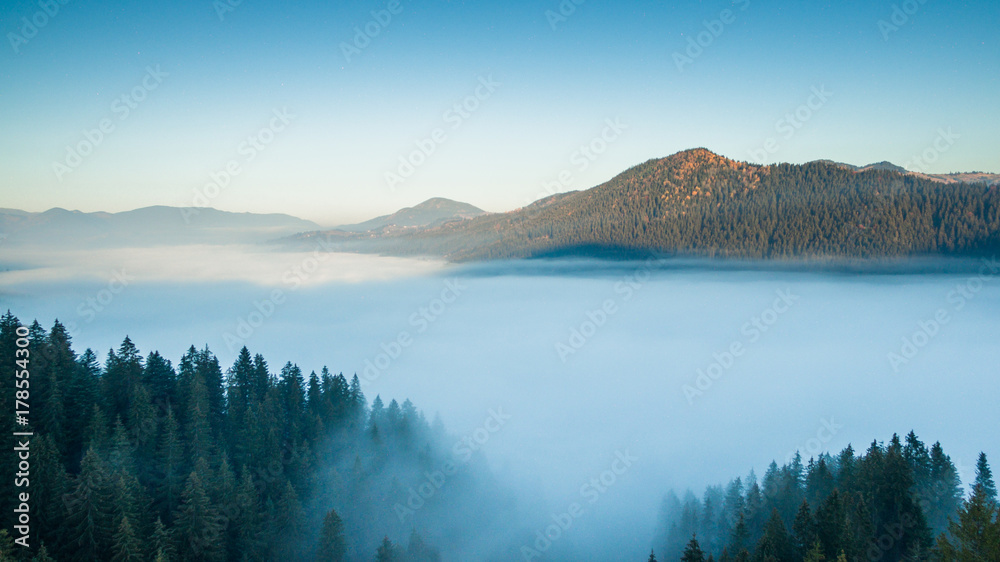 Aerial  view of the morning fog between the mountains.. Aerial landscape fog over the plain between the peaks of the mountains

