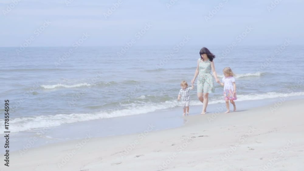 Happy family on the beach. Mother holds the arms of her son and daughter walking along the seashore. Slow motion.