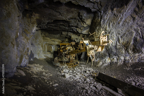 Underground abandoned ore mine shaft tunnel gallery with drilling machine rig
