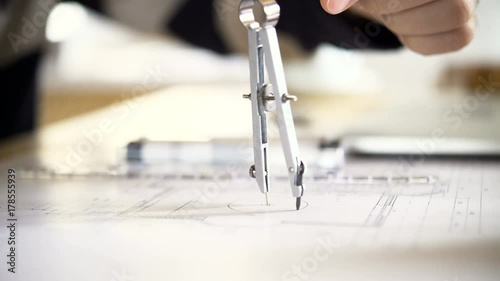 The architect draws a project of an apartment house using a pair of compasses. 4K video with shallow depth of field focus on objects.