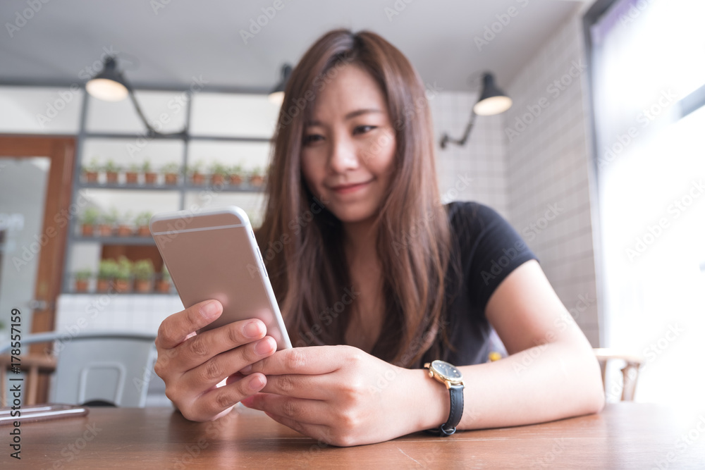 Closeup image of a beautiful Asian woman with smiley face holding and using smart phone in modern cafe Closeup image of a beautiful Asian woman with smiley face holding and using smart phone in modern cafe