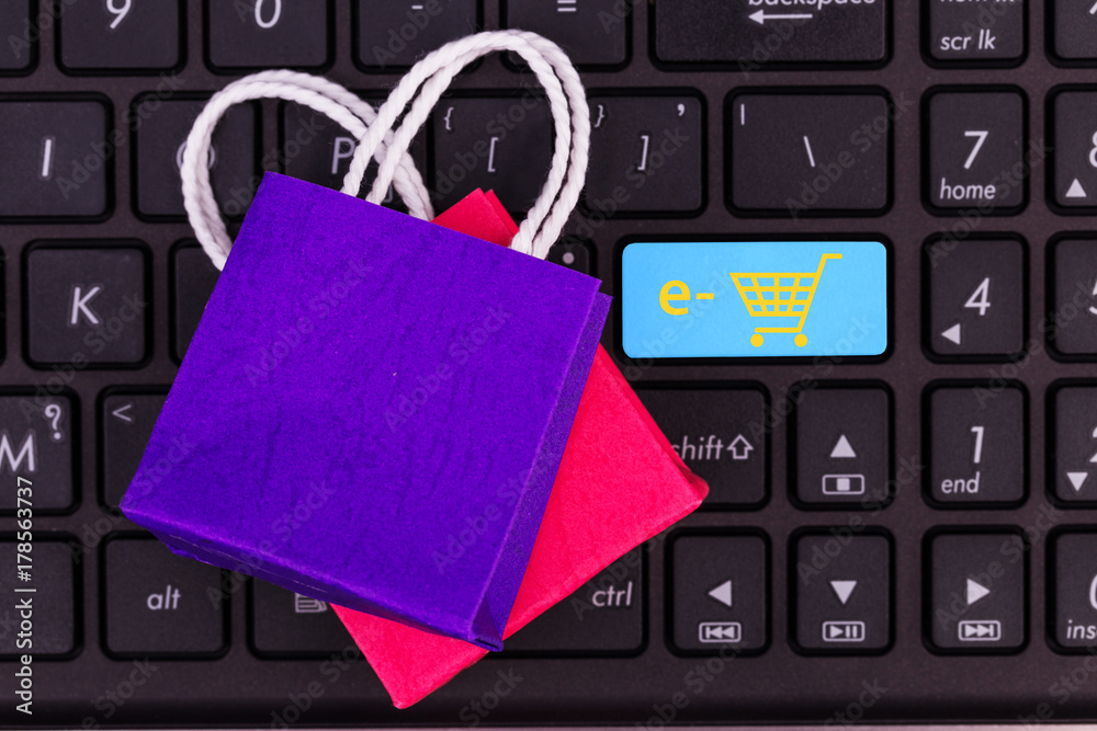 Small paper shopping bags on laptop keyboard.Is button waiting for customer / shopper to confirm and checkout.Online shopping,online digital money payment concept just search and clicks. Small paper shopping bags on laptop keyboard.Is button waiting for customer / shopper to confirm and checkout.Online shopping,online digital money payment concept just search and clicks.