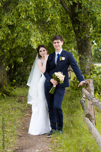 A beautiful married couple in wedding dresses, posing for a photo shooting in an belarusian village near the fence, with a wedding bouquet