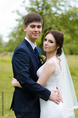 A beautiful married couple in wedding dresses, posing for a photo shooting in an belarusian village. Green background