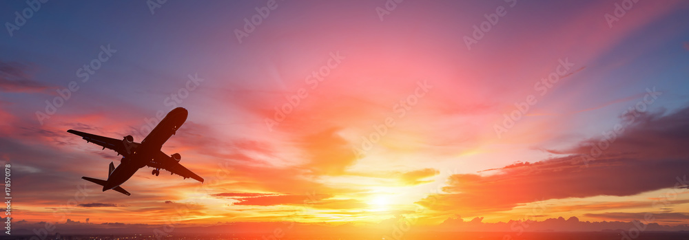 Obraz premium Sylwetka samolotu pasażerskiego latającego w zachodzie słońca.