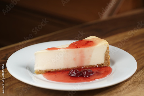 slice of traditional new york cheesecake with strawberry jam on white plate on wood table