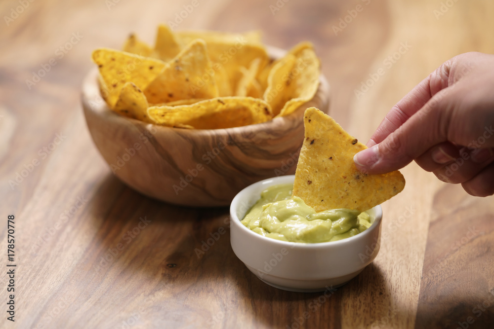 young female hand dipping nachos in guacamole sauce young female hand dipping nachos in guacamole sauce