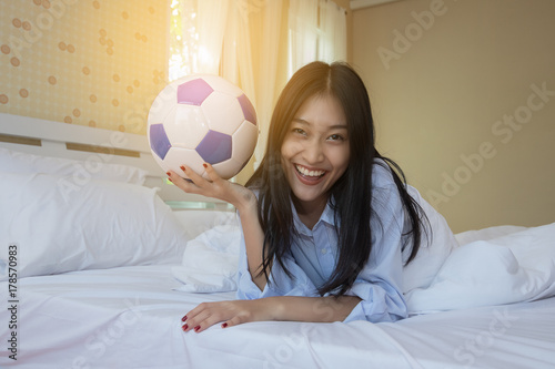 Woman is playing with a soccer ball in the bedroom.