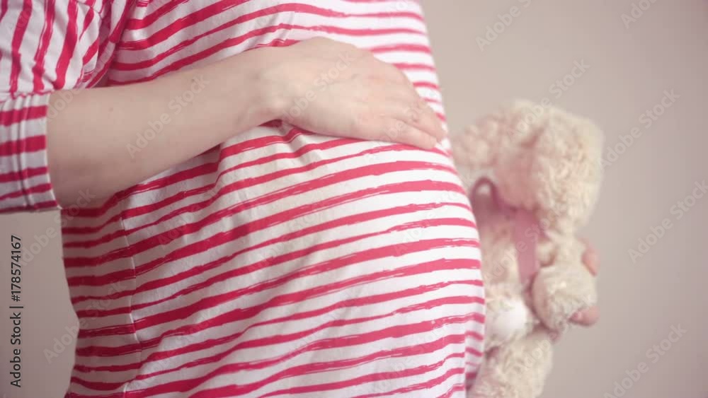Pregnant woman holding plush toy and touching her belly with hands Pregnant woman holding plush toy and touching her belly with hands