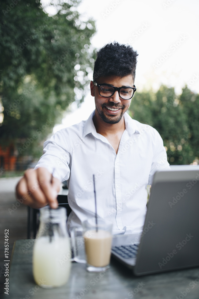 Positive and attractive Afro American businessman sitting in cafe bar doing some work on laptop Positive and attractive Afro American businessman sitting in cafe bar doing some work on laptop