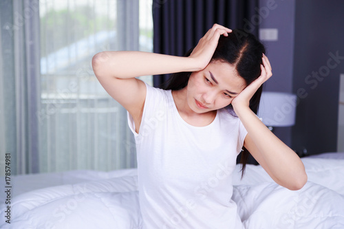 woman with headache on bed in bedroom