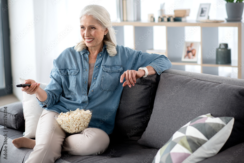 Fototapeta premium Joyful mature lady entertaining with television in living room