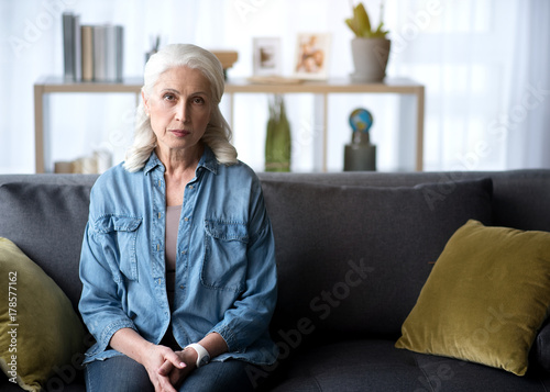 Serious mature lady locating on couch at home