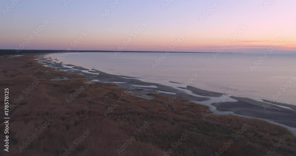 Aerial shot of coastal reed meadow at sunset aerial drone shot. Flying over yellow reed at sunset. Meadow grass on coastal area. Sand dunes in shallow water beach. Aerial shot of coastal reed meadow at sunset aerial drone shot. Flying over yellow reed at sunset. Meadow grass on coastal area. Sand dunes in shallow water beach.