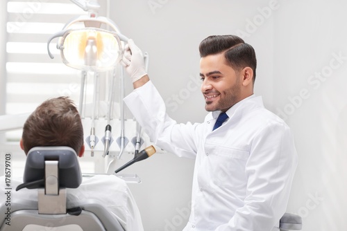 Cheerful young male dentist smiling at his male patient preparing for dental examination professionalism occupation work worker staff medicine health wellbeing dentistry concept.