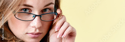 Beautiful redhead teenager girl with freckles wearing reading glasses, smiling teen portrait on yellow background