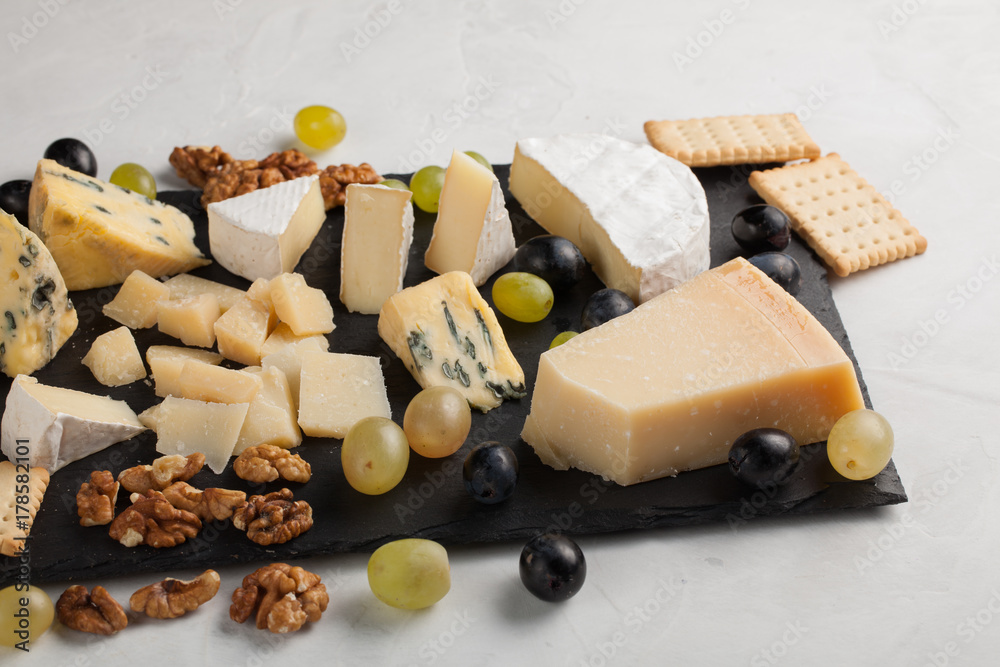 Assorted cheeses with white grapes, walnuts, crackers and on a stone Board. Food for a romantic date on a light background.