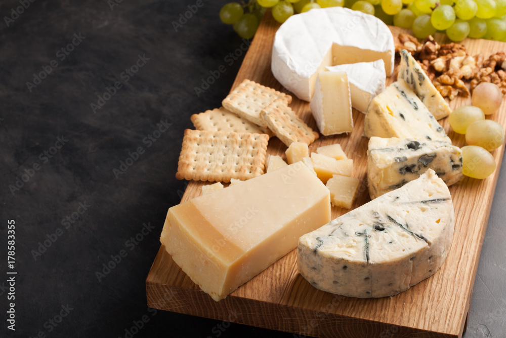 Fototapeta premium Tasting cheese dish on a wooden plate. Food for wine and romantic, cheese delicatessen on a dark stone table. with copy space