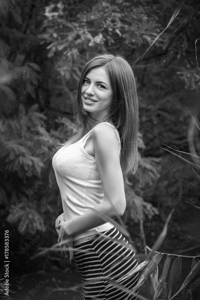 Black and white portrait of beautiful young smiling woman with long hair, wearing long striped skirt and white top standing in a forest Black and white portrait of beautiful young smiling woman with long hair, wearing long striped skirt and white top standing in a forest
