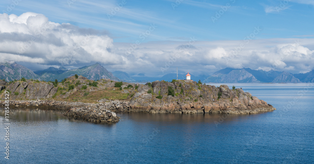 Naklejka premium Lighthouse on a rocky cape on a background of mountains, Lofoten, Norway