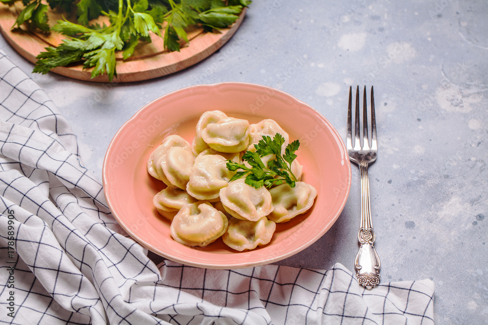 Boiled dumplings in a pink plate on a gray background, parsley, horizontal