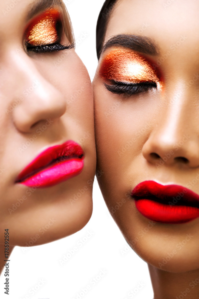 Close-up of faces of two women with bright makeup, pink lips, orange colorful metallic eyeshadows, closed eyes. Cosmetics, well-groomed skin, white isolated background Close-up of faces of two women with bright makeup, pink lips, orange colorful metallic eyeshadows, closed eyes. Cosmetics, well-groomed skin, white isolated background